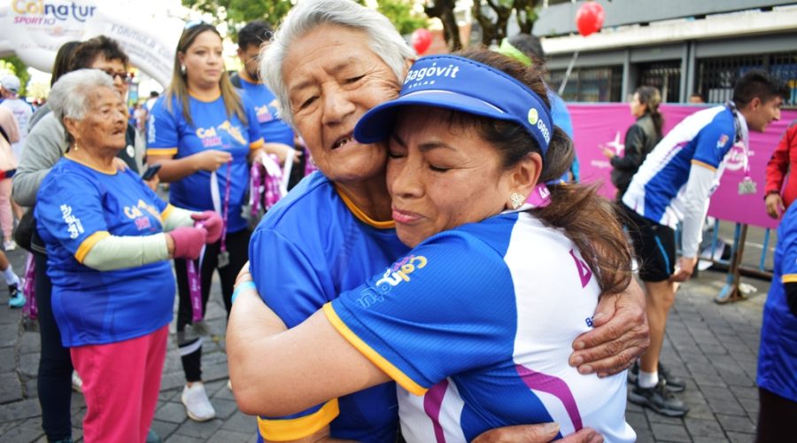 Corredora emocionada recibe la medalla de manos de Clemencia, beneficiaria del Centro para el Adulto Mayor